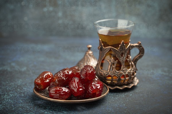 Breaking fasting with dried dates during Ramadan Kareem, Iftar meal with dates and Arab tea in traditional glass, angle view on rustic blue background. Muslim feast, food photography, food photography
