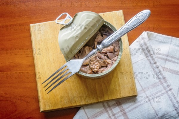 An open tuna box on a wooden board, with a fork and a towel