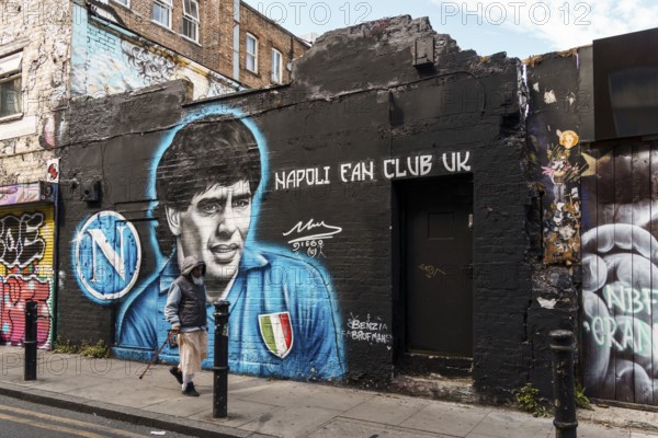 London, UK, August 25, 2023: Street scene with people walking by Brick Lane in Shoreditch Area in the East End. Maradona graffiti painted on walk on background