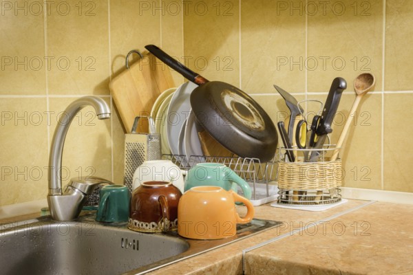 Dishes, cups, glasses, plates, forks, knives and spoons are drying close to the sink, after they have been washed in kitchen