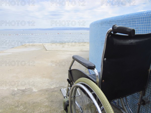 Empty wheelchair on an accessible beach with pool for assistance to help people with disabilities into the water