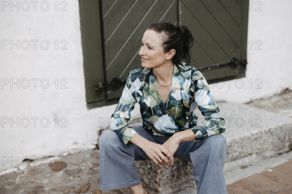 Smiling, dark-haired woman, 40+, sitting on a staircase