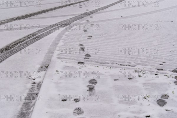 Fresh snow covers a cobblestone street with footprints and tire tracks crossing, creating a winter urban scene