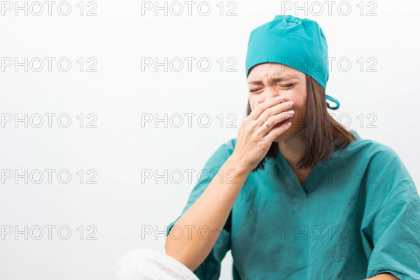 Emotional nurse in teal uniform crying on a white background