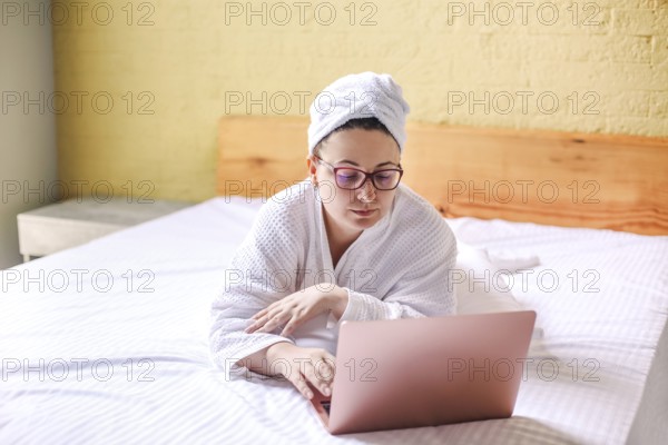 Happy woman in eyeglasses waiting and has video call on laptop lying on bed. Work from home concept