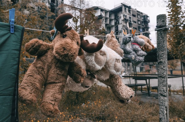 Soft toys are dried after washing against the background of a burnt-out multi-storey building in Mariupol