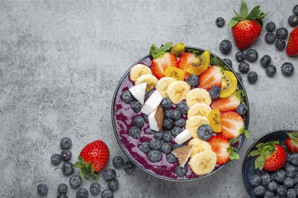 Healthy summer acai smoothie bowl with chia seeds, fresh banana, strawberry, blueberry, cocos, kiwi top view on rustic concrete background with spoon. Space for text, food photography, food photography