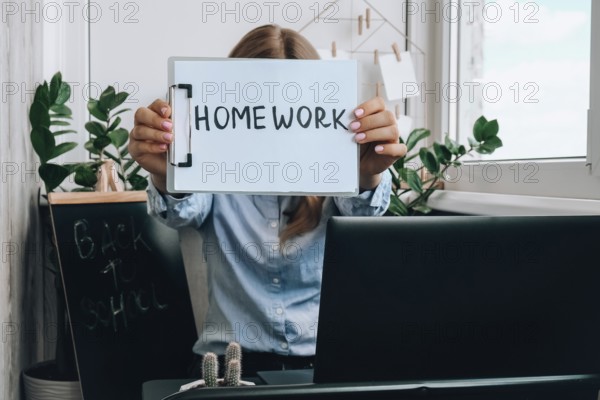 Young female teacher sitting at desk and using laptop showing HOMEWORK text at home. e Education Back to school. Student learning online class. Distance learning. Exam preparation Lockdown quarantine new normal