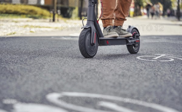 Young man in casual trousers riding an electric scooter detail on his feet and wheel over asphalt road, Liptovsky Mikulas, Slovakia, Europe