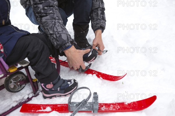 Dad helps his little daughter to put on children's plastic skis. Sports training, skiing, support and assistance. Winter active sports outdoor since childhood