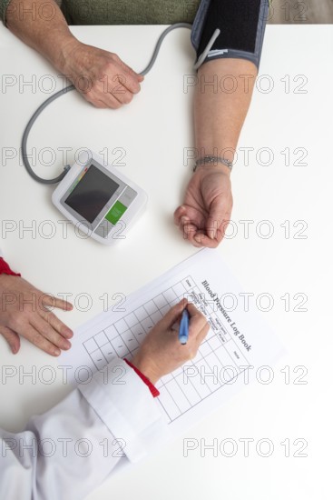 Doctor taking notes on blood pressure log book while measuring blood pressure of senior woman patient