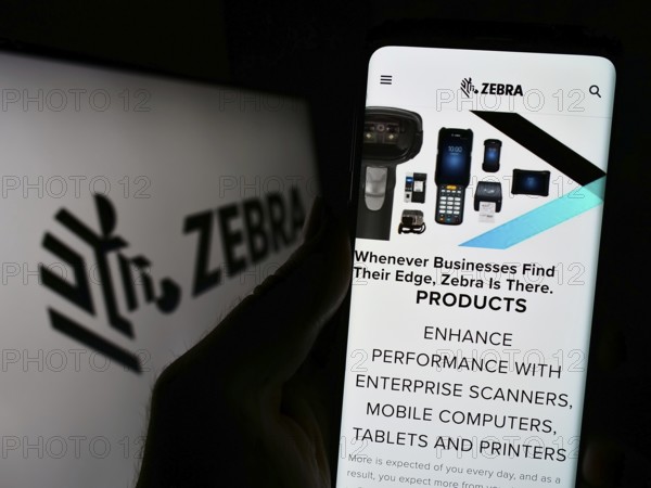 Stuttgart, Germany, 08-13-2023: Person holding cellphone with webpage of US company Zebra Technologies Corporation on screen in front of logo. Focus on center of phone display, Europe