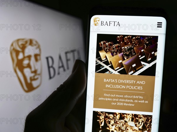 Stuttgart, Germany, 07-14-2023: Person holding cellphone with webpage of British Academy Film Awards (BAFTA) on screen in front of logo. Focus on center of phone display, Europe
