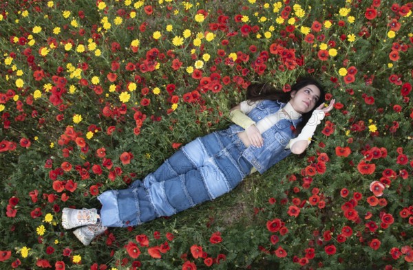 Young happy girl resting in the field of red poppy flowers. Drone aerial of woman in spring