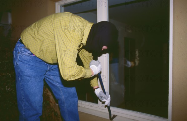 A masked burglar breaks into a house at night with a crowbar