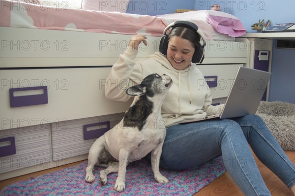 A teenager enjoys a moment of leisure in her room, working on her laptop and playing with her dog, creating an atmosphere of tranquility and happiness, tarragona, spain