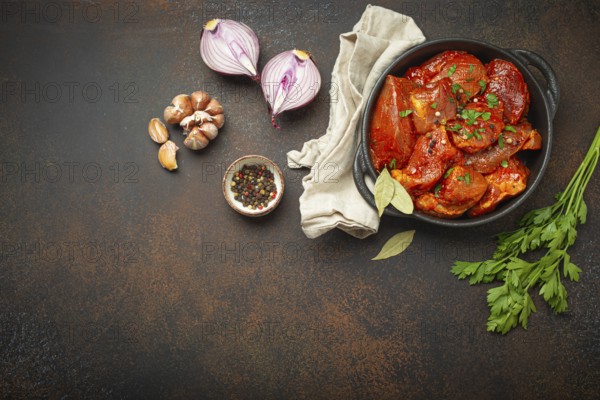 Cooking hearty meat stew. Raw uncooked chopped pieces of meat marinated with seasonings and parsley in black casserole dish top view, ingredients on dark rustic background. Space for text, food photography, food photography