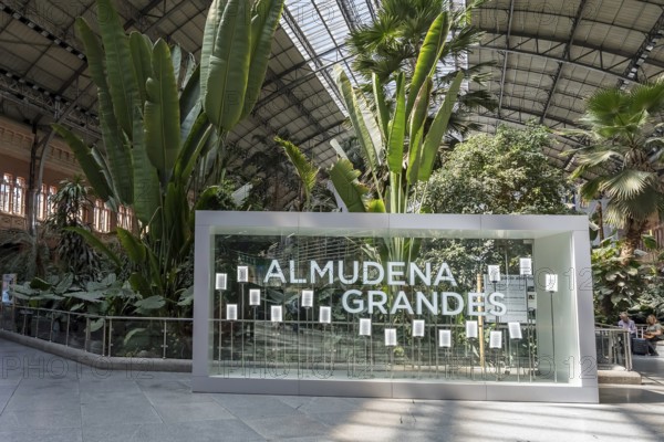At Almudena Madrid's Puerta de Atocha?Almudena Grandes station, commuters await trains amidst bustling crowds, immersed in the vibrant rhythm of urban life