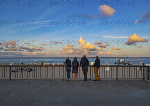 Holidaymakers stand on the promenade in the evening light and look out to sea, Hörnum, Sylt