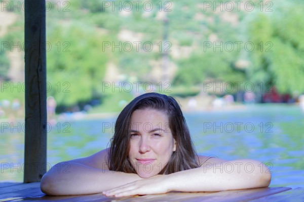 Beautiful brunette woman bathing in a lake perched on a wooden pontoon looking at the camera with a smile on her face