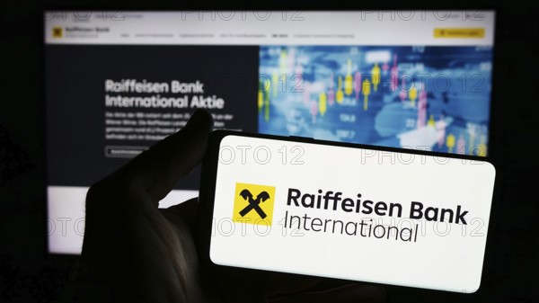 Stuttgart, Germany, 03-16-2024: Person holding smartphone with logo of Austrian company Raiffeisen Bank International AG (RBI) in front of website. Focus on phone display, Europe