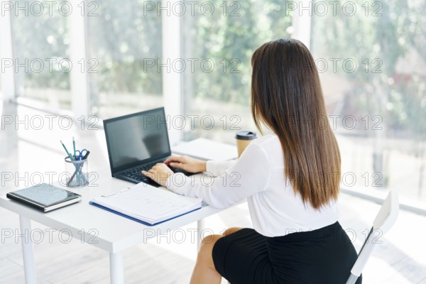Back view of young businesswoman working with laptop in modern office