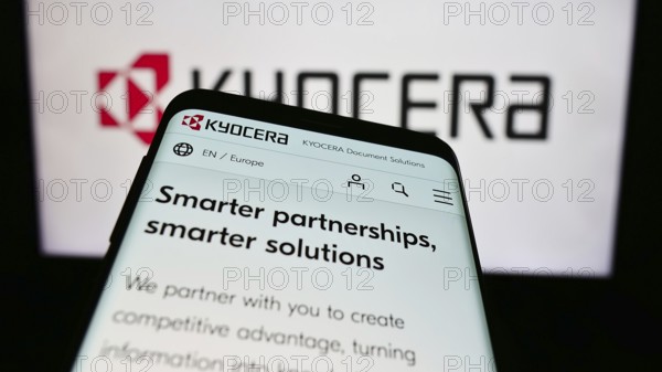 Stuttgart, Germany, 02-08-2024: Mobile phone with website of Japanese electronics company Kyocera Corporation in front of business logo. Focus on top-left of phone display, Europe