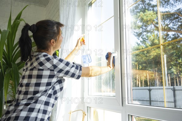 Woman manually washes the window of the house with a rag with spray cleaner and mop inside the interior with white curtains. Restoring order and cleanliness in the spring, cleaning servise