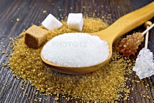Sugar white and brown in cubes, crystal on a stick and granulated in a spoon on a wooden plank background