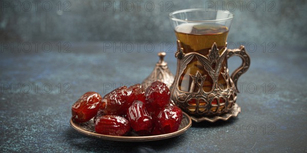 Breaking fasting with dried dates during Ramadan Kareem, Iftar meal with dates and Arab tea in traditional glass, angle view on rustic blue background. Muslim feast, food photography, food photography