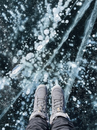 Fragile thin brittle ice underfoot. Female feet on ice. Woman wearing winter shoes on ice of Baikal, Russia. Cracks on ice background. Ice of Lake Baikal. Holiday and travel concept