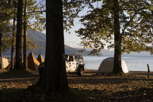 Tents and a white jeep with mountains in the background, sunrise at the lake, Shikotsu-Lakeside Bifue campsite, Japan, Asia