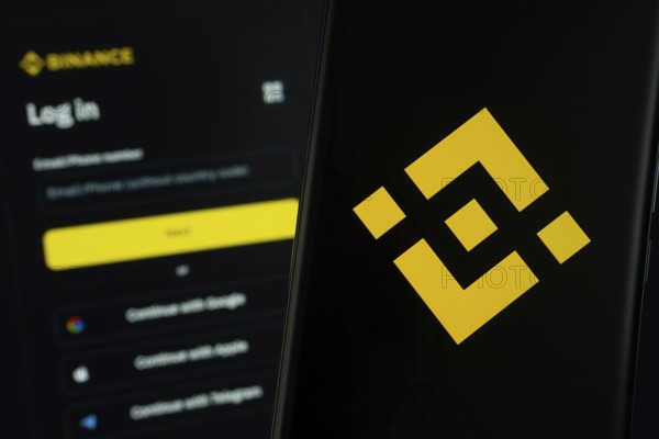 Binance logo is displayed on a smartphone screen, with the binance login page visible on a computer screen in the background