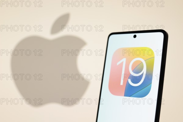 In this photo illustration, the iOS 19 logo seen displayed on a smartphone with an Apple logo in the background