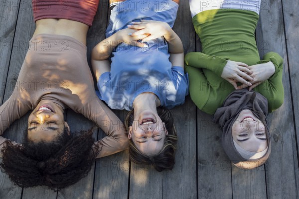 Multiracial young teen female friends resting in the park after sport training laughing and having fun together. Diversity, sport and friendship concept