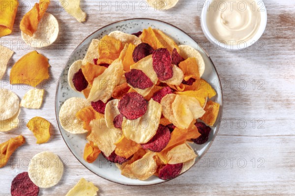 Various vegetable chips with a homemade dip, shot from the top on a rustic wooden background with a place for text
