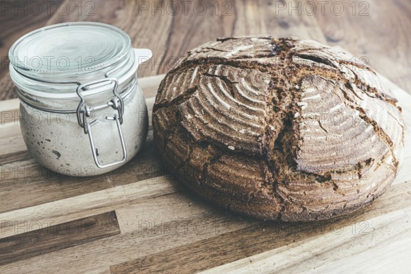 Freshly baked homemade rye sourdough bread and sourdough starter in jar on wooden table