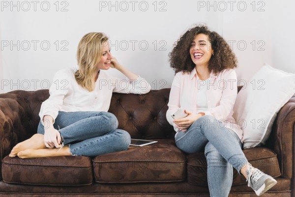 Cheerful women with technologies speaking sofa