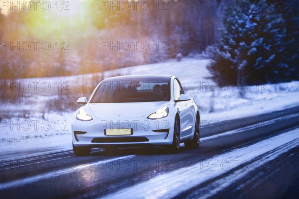 White Tesla Model 3 electric car at speed on highway in winter at dusk. Salo, Finland. December 27, 2021