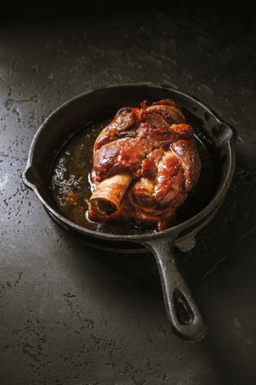 Traditional German cuisine - Roasted pork knuckle eisbein (Schweinshaxe) in iron pan on black background