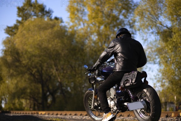 Male motorcyclist in a leather jacket and helmet on a vintage custom motorcycle in nature. Concept of motorcycle life and the beginning of the season