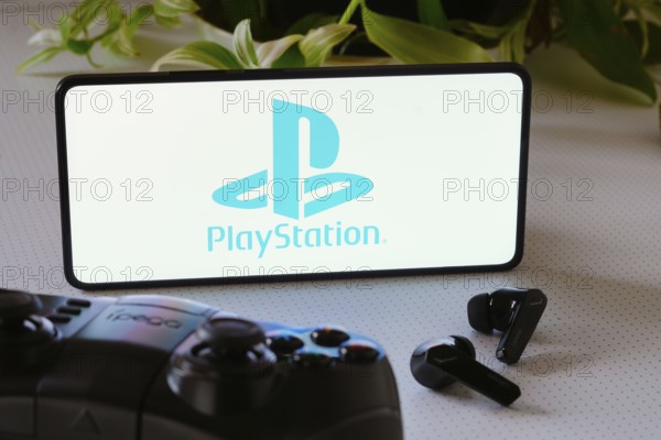 In this photo illustration, the PlayStation logo is displayed on a smartphone screen, next to a gamepad and headphones