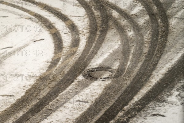 Car tire tracks curving on a snowy road surface in winter, indicating vehicle movement and winter driving conditions