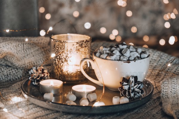 Cup with hot winter cacao and marshmallows on bed. Christmas lights. Pine cones decoration. Cozy winter days. Hygge