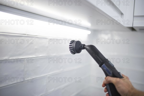 Steam cleaner with a brush scrubbing white kitchen tiles