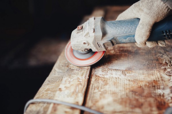 Close-up of an angle grinder being used on a wooden table by a gloved hand