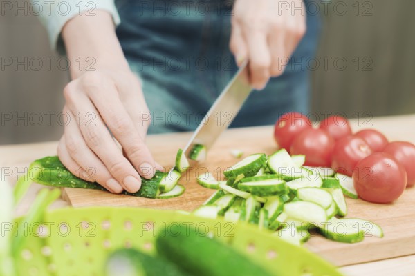 Close-up of female hands cut into fresh cut cucumbers on a wooden cutting board next to pink tomatoes. The concept of homemade vegetarian cuisine and healthy eating and lifestyle