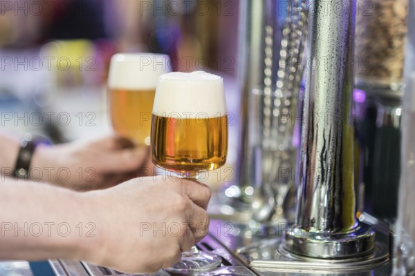 Barman picking up Two beer glasses in the tap of a pub