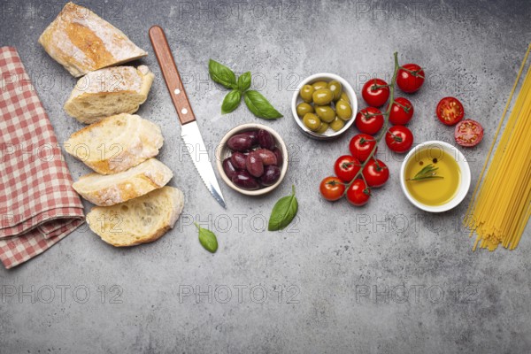 Food composition with sliced ciabatta, olives, olive oil, spaghetti, fresh basil, cherry tomatoes on gray concrete stone rustic background top view, copy space. Italian cuisine concept, food photography, food photography