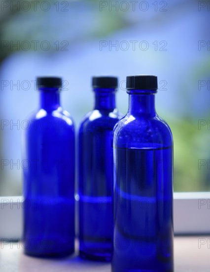 Three Blue glass body oil bottles in bathroom window